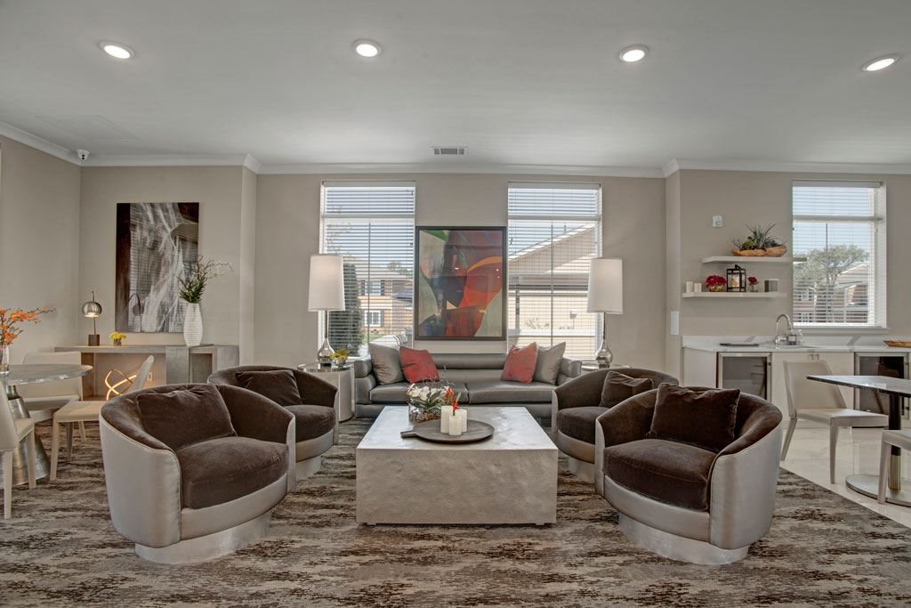A stylish community lounge here at Indigo with plush seating, modern lighting, and large windows bringing in natural light. A nearby kitchen and dining area create a comfortable and inviting space for relaxing or gathering.